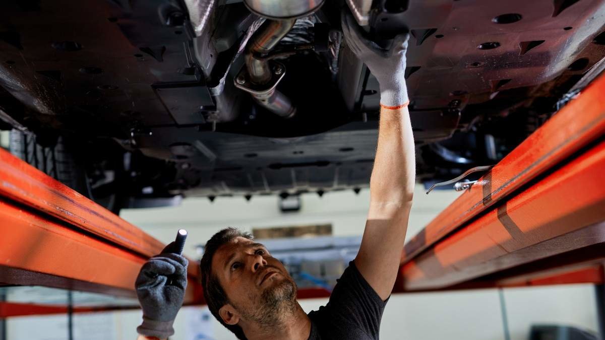 Auto repairman examining undercarriage of a car in a workshop.